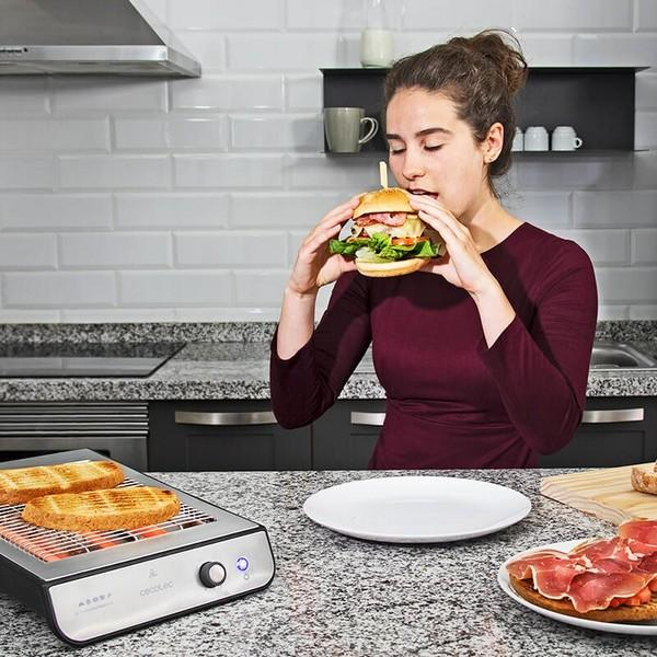 Een vrouw die een burger eet naast een grill met toast en een bord met ham.