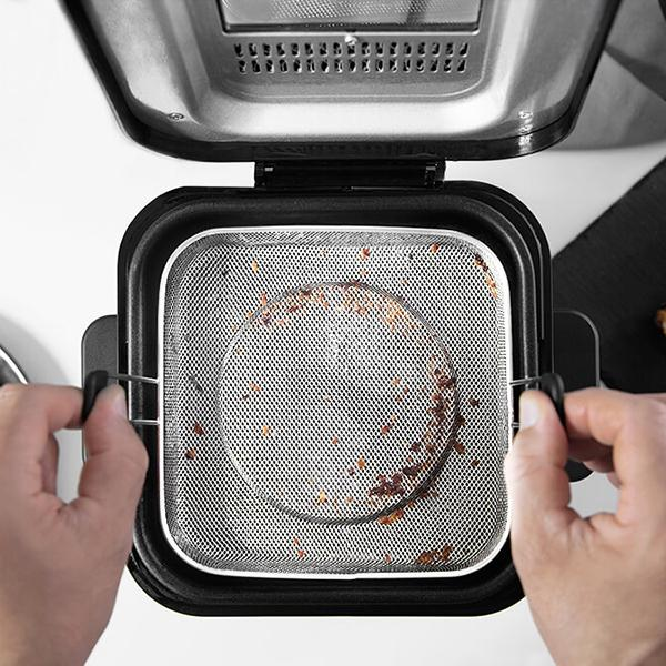 Osoba trzymająca urządzenie do gotowania z koszem z siatki ze stali nierdzewnej. Urządzenie jest otwarte.
