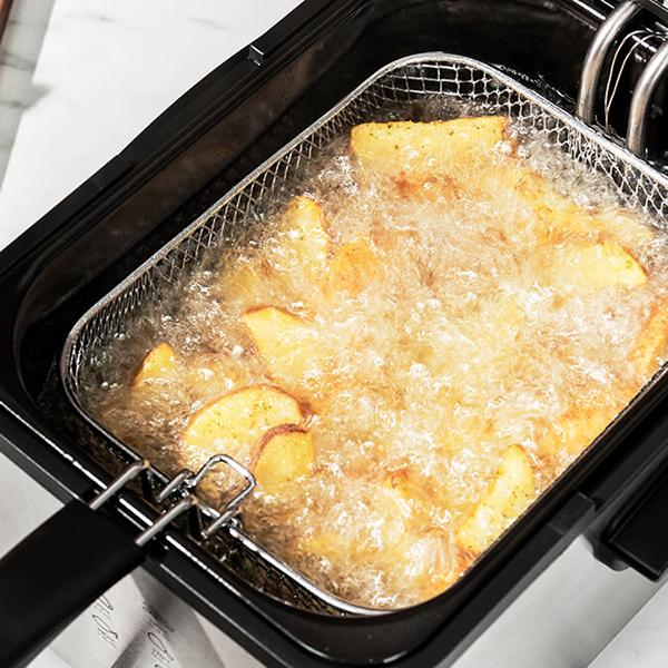 Nahaufnahme von Pommes Frites, die in heißem Öl in einer Fritteuse frittiert werden, mit einem Netzkorb.