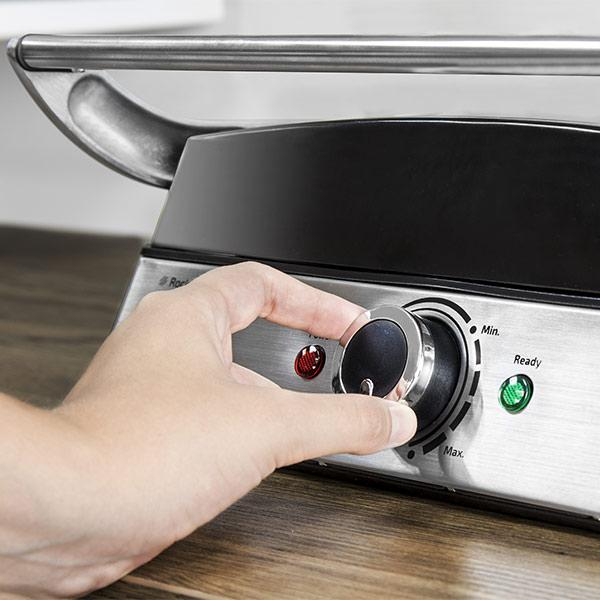 Dłoń kręci pokrętłem na srebrnej płycie grillowej. Pokrętło jest czarne. Widoczne czerwone i zielone światło.