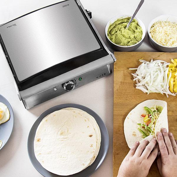 Grill, tortille, guacamole, ser i posiekane warzywa. Ręce zawijają tortillę.