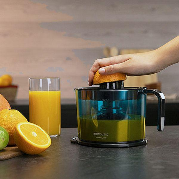 Una mano femminile che sprema un'arancia in uno spremiagrumi. Presenti bicchiere di succo e arance.