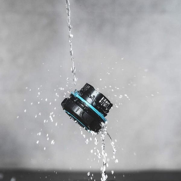 Schwarz-blaues Kameraobjektiv, das mit Wasser bespritzt wird, grauer Hintergrund.