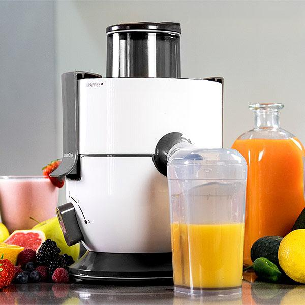 Estrattore di succo con un bicchiere e una bottiglia di succo, con frutta intorno. Estrattore bianco, succo d'arancia.