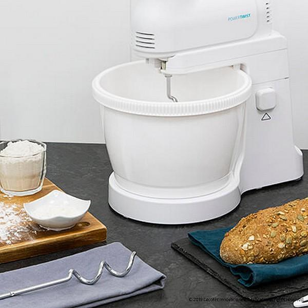 Batidora de pie blanca con bol, accesorios e ingredientes en mostrador. Pan cerca.