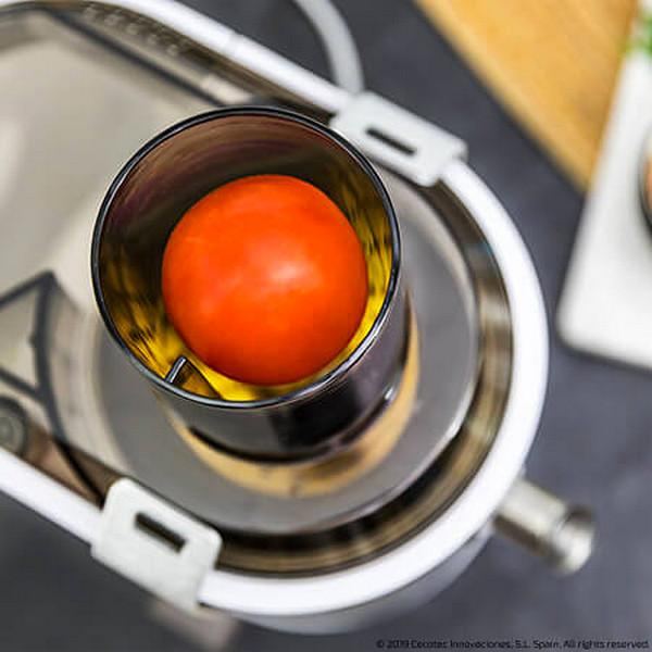 Un tomate dentro de un procesador de alimentos con un recipiente de acero inoxidable. El procesador es blanco.