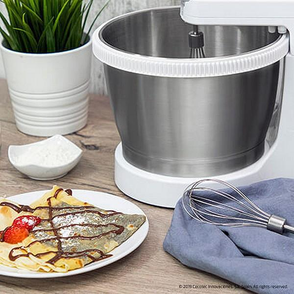 Ein Teller mit Crêpe mit Schokolade und Erdbeeren. Ein Mixer und eine Schüssel mit Mehl. Holzoberfläche.