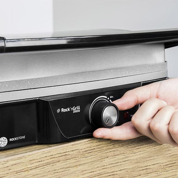 Ręka kręci pokrętłem na grillu. Grill jest czarny i srebrny. Widoczne logo Rock'n'Grill.