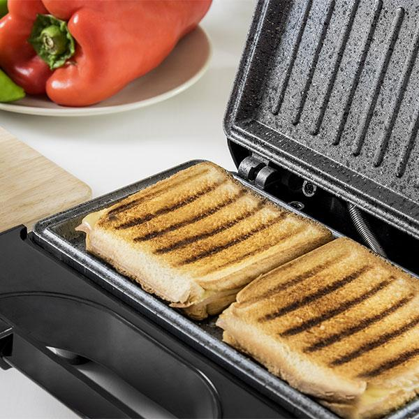 Panini nella pressa, con peperoni rossi e un piatto bianco sullo sfondo.