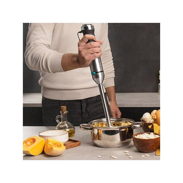 Persoon die ingrediënten mengt in een pan met een zilveren staafmixer.