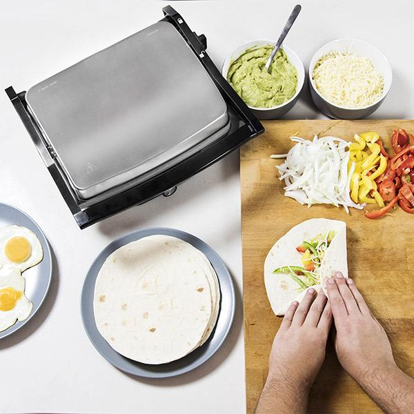 Jedzenie jest przygotowywane. Płyta grillowa ze składnikami i narzędziami. Osoba przygotowuje jedzenie.