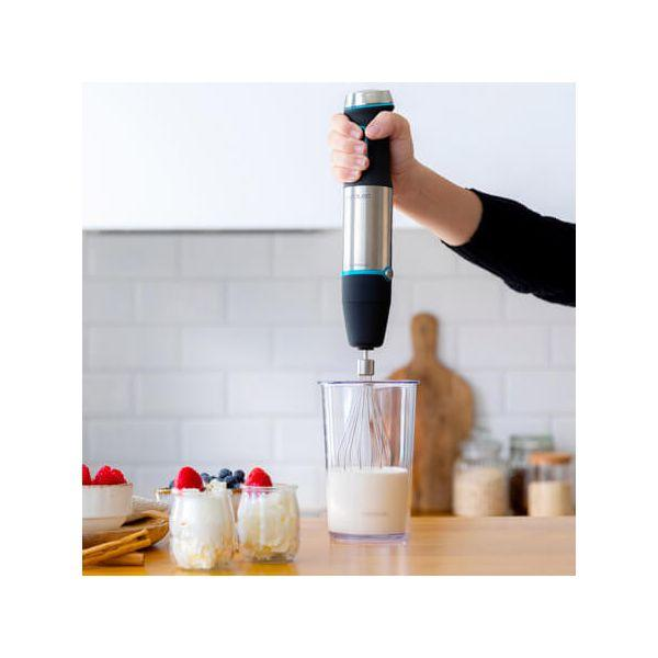 Een hand houdt een zilver-zwarte staafmixer boven een glas met melk.