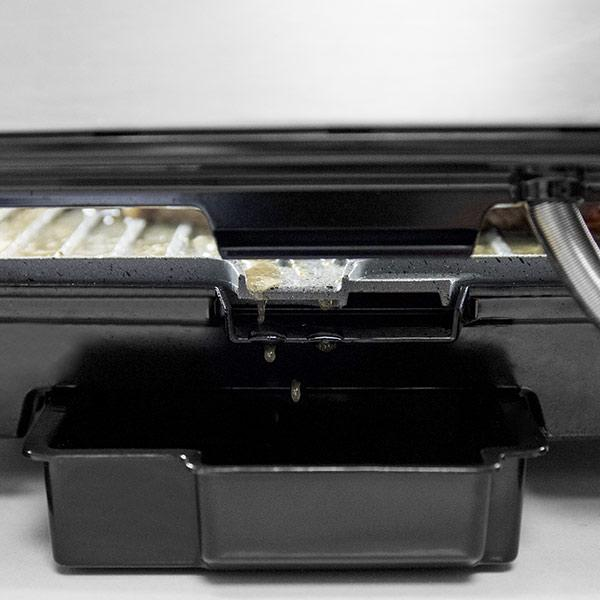 Zbliżenie czarnego grilla z olejem kapiącym do czarnej tacy.