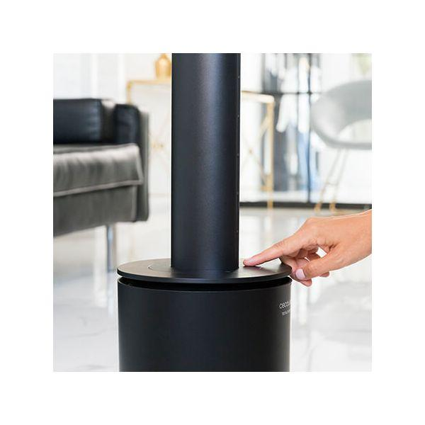 Un dito preme un pulsante su un ventilatore nero, cilindrico e da terra.