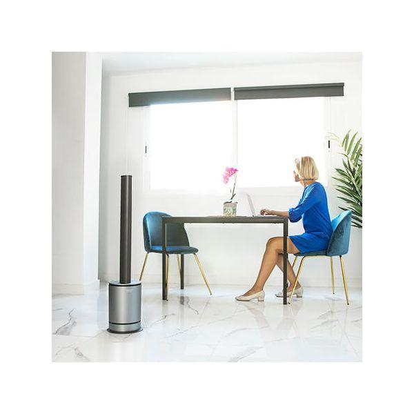 Donna che lavora al laptop alla scrivania, con ventilatore. Interni moderni.