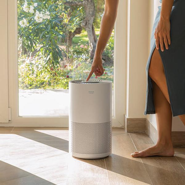 Una donna tocca un purificatore d'aria bianco. Dietro di lei c'è una finestra che mostra il fogliame.