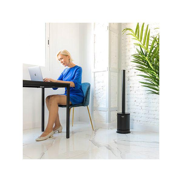 Una donna che lavora su un laptop a un tavolo, con un termoventilatore nero di lato.
