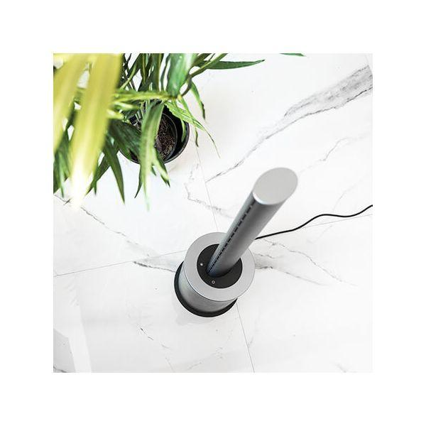 Un ventilatore argento e nero su un pavimento di marmo bianco con una pianta sullo sfondo.