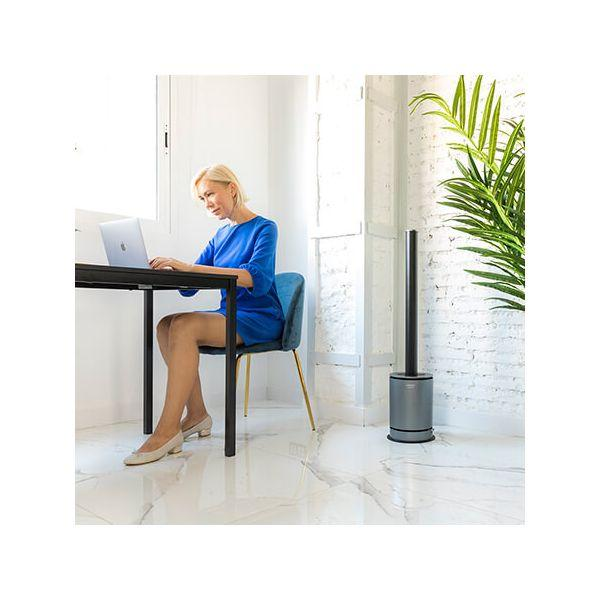 Una donna in abito blu usa un laptop su una scrivania. C'è un ventilatore accanto a lei.