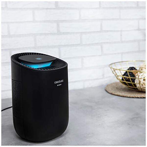 Czarny oczyszczacz powietrza na szarym blacie. Biała ceglana ściana w tle. Złoty kosz po prawej stronie.