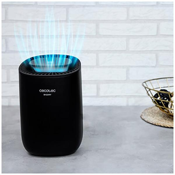 Czarny oczyszczacz powietrza z niebieskim światłem emitowanym z góry. Biała ceglana ściana w tle.