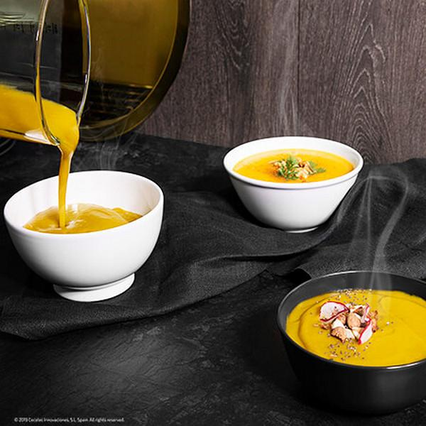 Tres cuencos de sopa, con sopa vertiéndose de una jarra. La sopa es amarilla y el fondo es oscuro.