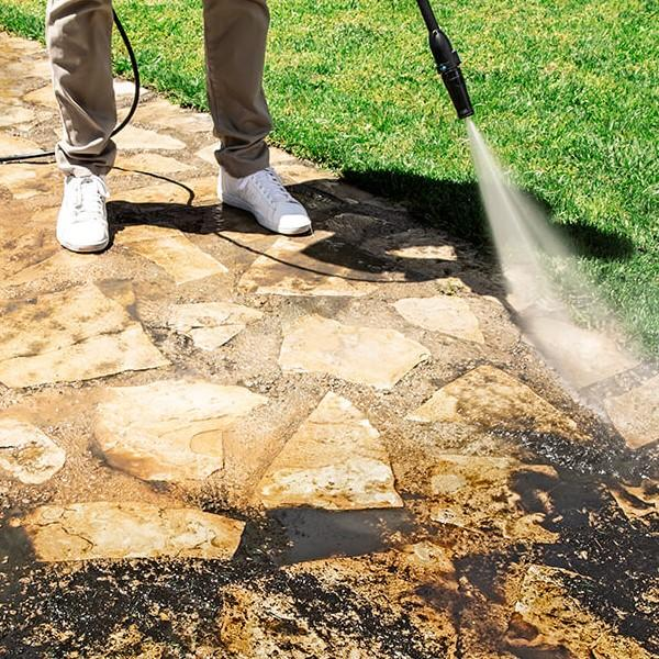 Una persona lavando un patio de piedra con una hidrolavadora, creando una franja limpia.