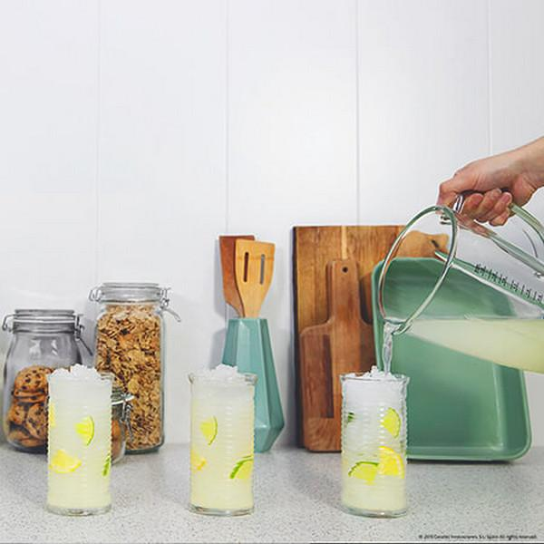 Limonata versata in bicchieri con ghiaccio. Barattoli, assi di legno e utensili sul bancone.