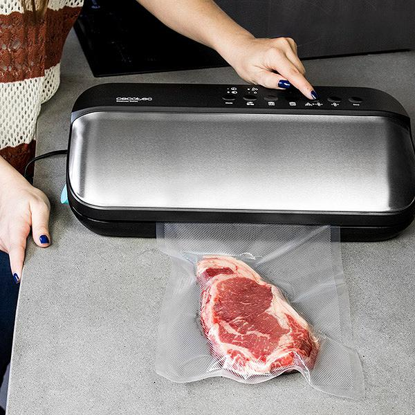 Kobieta używa zgrzewarki próżniowej na blacie. Surowy stek znajduje się w zamkniętej torbie.