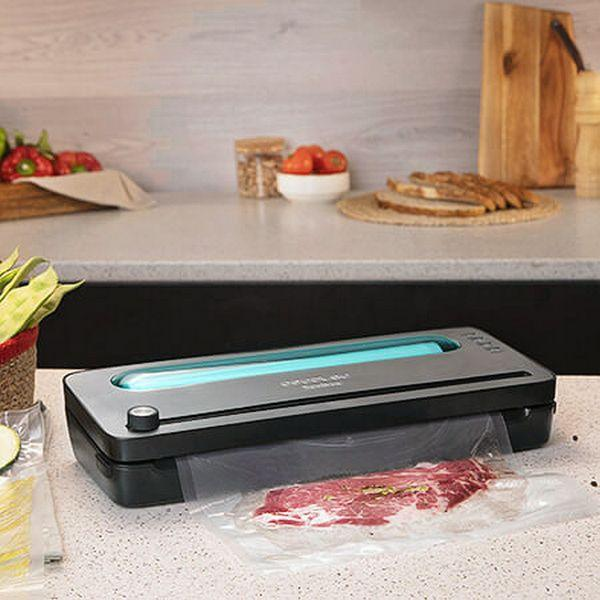 Eine schwarz-graue Vakuumversiegelungsmaschine. Auf der Maschine befindet sich ein Beutel mit Fleisch.
