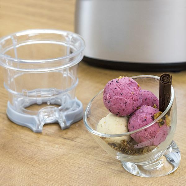 Un bol de vidrio con bolas de helado y un palito de chocolate. Junto a él, un contenedor de helado.
