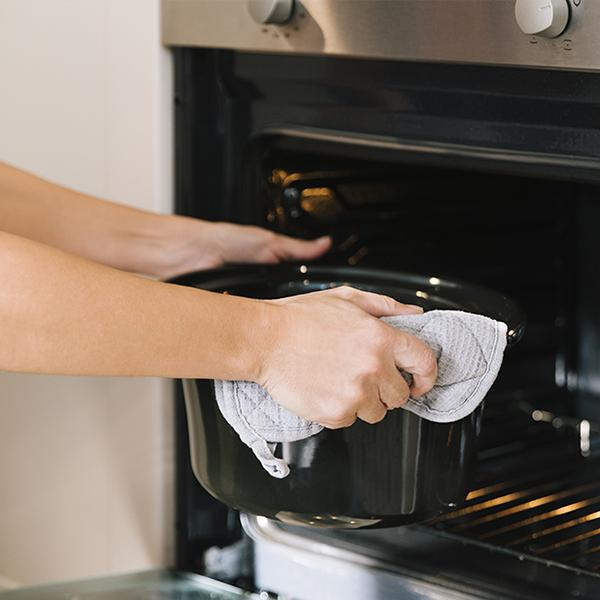 Manos con un guante de horno gris, colocando una olla negra en un horno caliente.