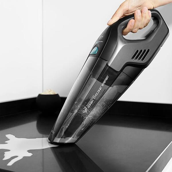 Un aspirateur à main sur une surface noire, avec du liquide blanc renversé, près d'un bol noir.