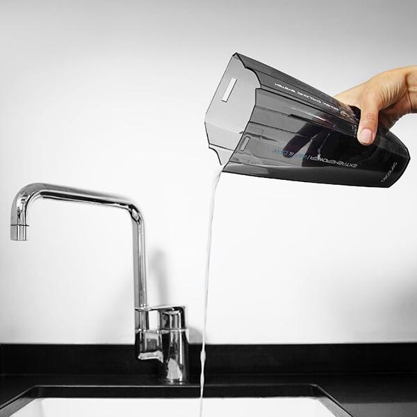 La main verse de l'eau d'un récipient d'aspirateur noir dans un évier.