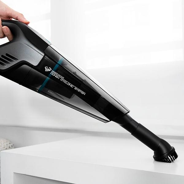 Aspirateur à main noir et gris, tenu au-dessus d'une surface blanche.