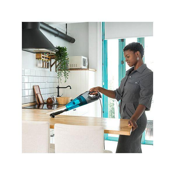 Una donna che aspira un bancone di legno con un aspirapolvere portatile blu e nero in una cucina.