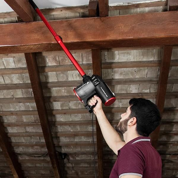 Un uomo che aspira un soffitto di legno con un aspirapolvere rosso e nero.