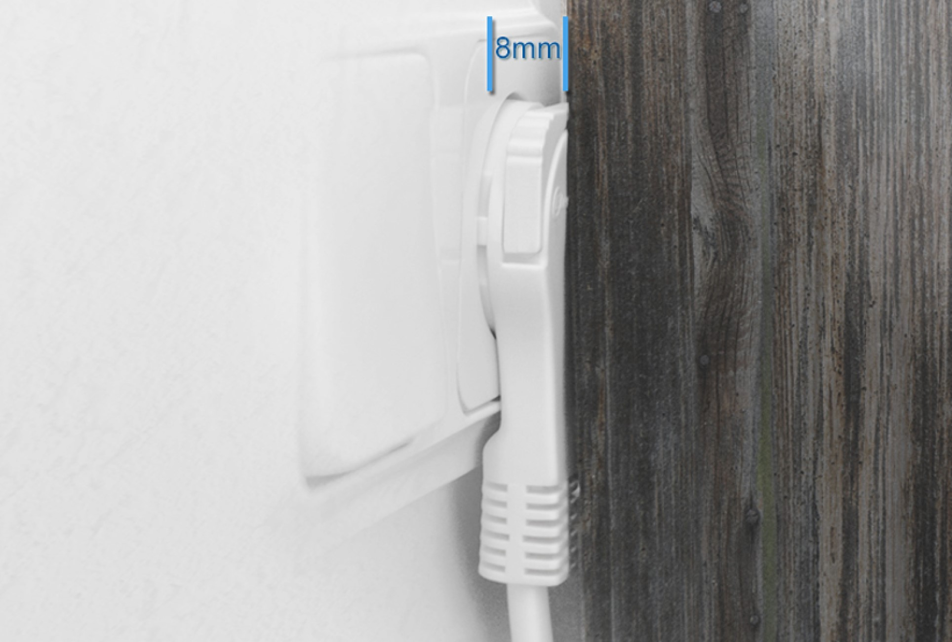 Ein weißer Stecker, der in eine Steckdose gesteckt wird. Die Wand ist weiß, und eine Holzverkleidung grenzt an.