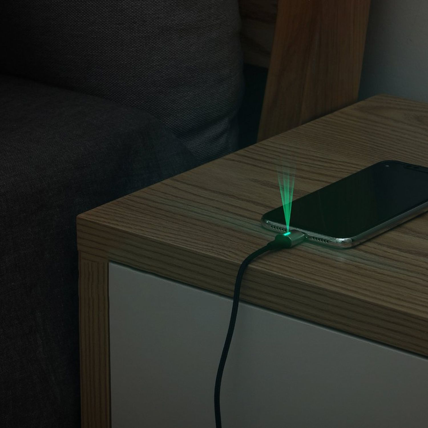 Ein Telefon, das auf einem Nachttisch aus Holz geladen wird. Ein grünes Licht geht vom Ladeanschluss aus.