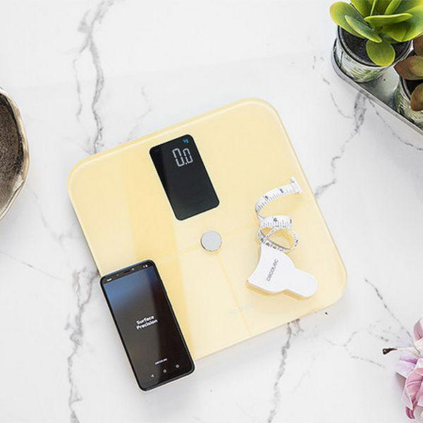 Waga z telefonem i miarką na białej marmurowej powierzchni. Roślina w tle.