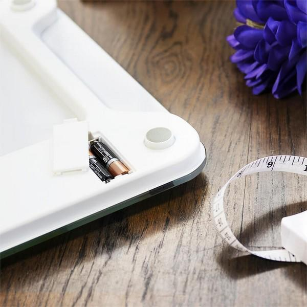 Biała waga z bateriami i miarką na drewnianej powierzchni, fioletowy kwiat.