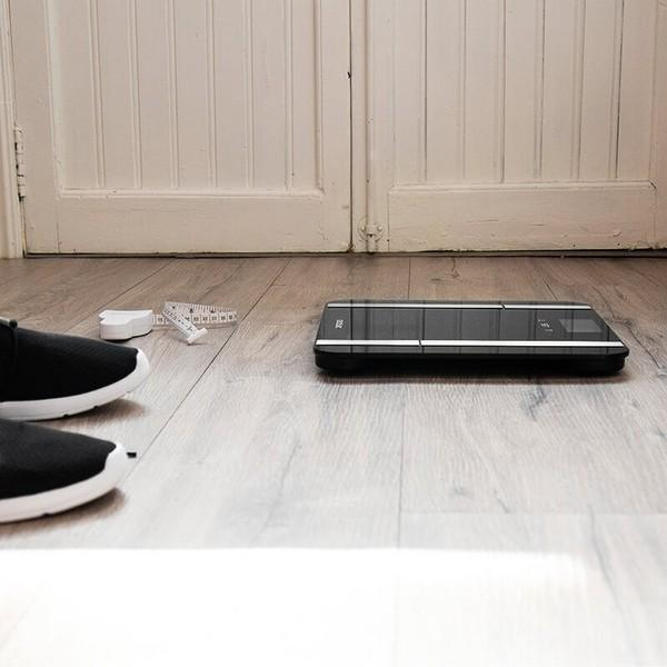 Inteligentna waga i miarka na drewnianej podłodze, ze stopami osoby w kadrze.