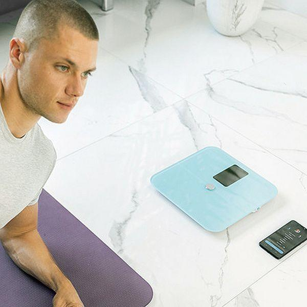 Un hombre mira una báscula junto a una esterilla de yoga y un teléfono inteligente.