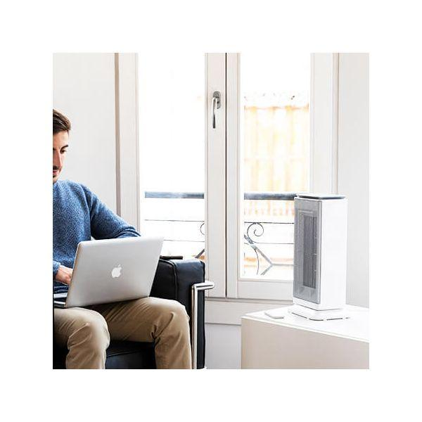 Mężczyzna z laptopem, biały grzejnik na stole, okno w tle.