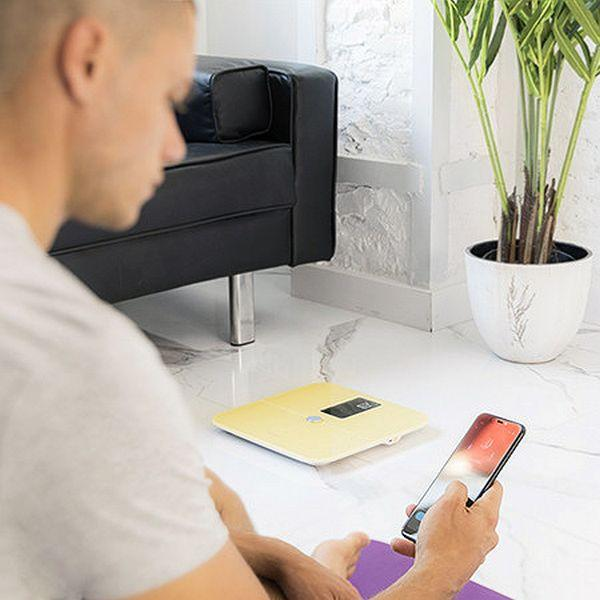 Mężczyzna siedzi z telefonem, patrząc na wagę. Czarne kanapa i roślina w tle.