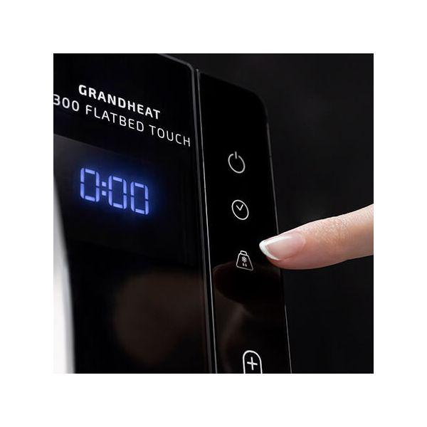 Pannello di controllo di un elettrodomestico nero con orologio digitale e pulsanti touch, un dito tocca un pulsante.