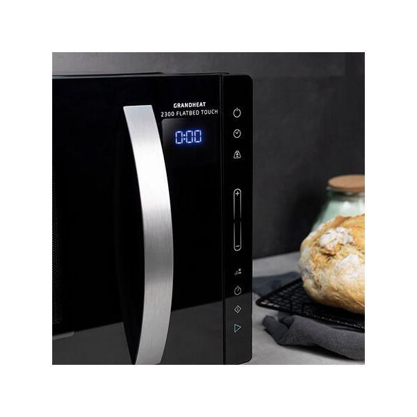 Forno a microonde nero con maniglia argentata e display digitale 0:00. Pane nelle vicinanze.