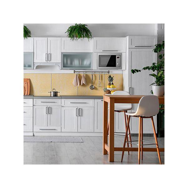 Biała kuchnia z szafkami, kuchenką mikrofalową i stołem barowym z krzesłami. Żółte płytki.