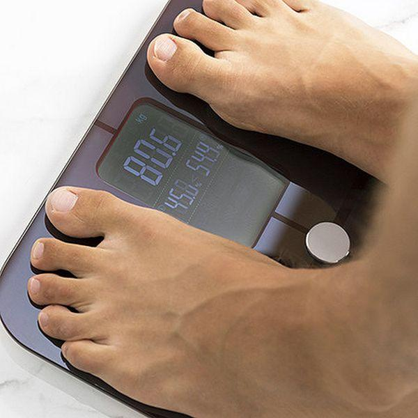 Füße auf einer digitalen Waage, die 80,6 kg und andere Gewichtsdetails anzeigt.