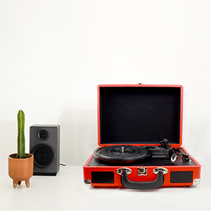 Czerwony przenośny gramofon z kaktusem i głośnikiem na białej powierzchni.